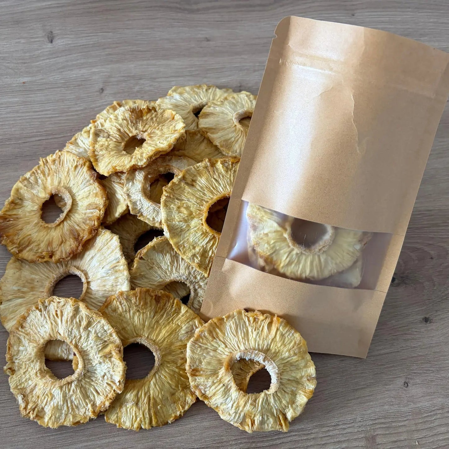 atural dried pineapple rings with fibrous texture and golden color, displayed next to an eco-friendly kraft paper pouch on a wooden surface.