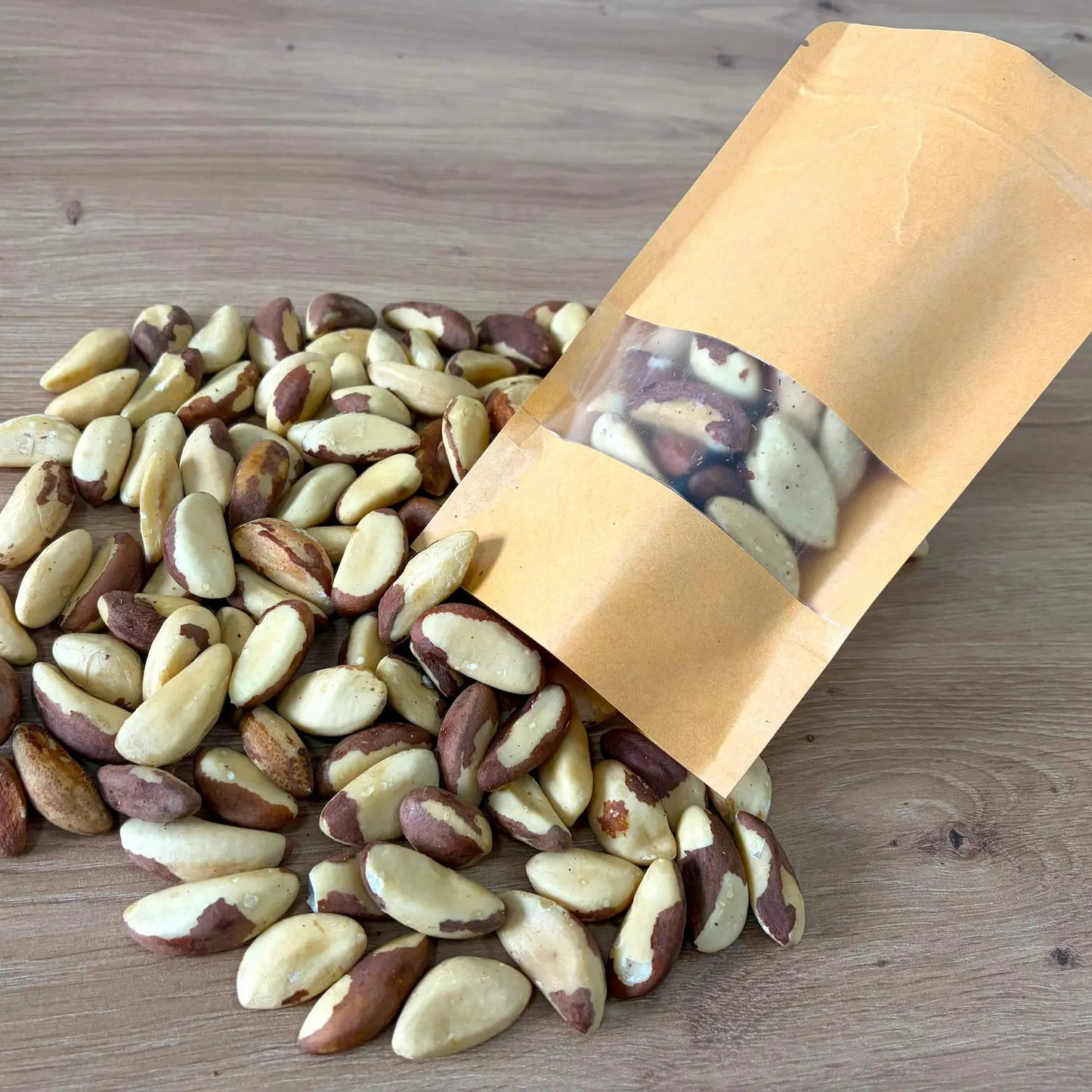 Large raw Brazil nuts, rich in selenium, displayed next to an eco-friendly kraft paper pouch on a light wooden surface.