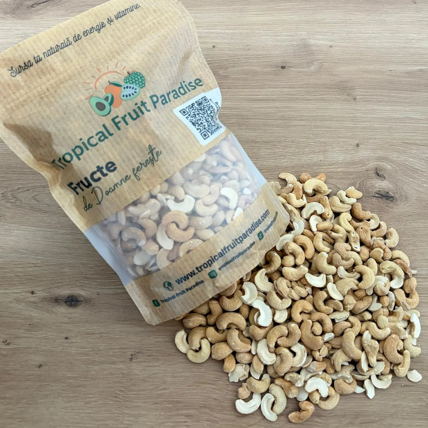 Premium roasted cashews with a warm golden-cream hue, spilling out from a branded Tropical Fruit Paradise kraft pouch onto a light wooden table.