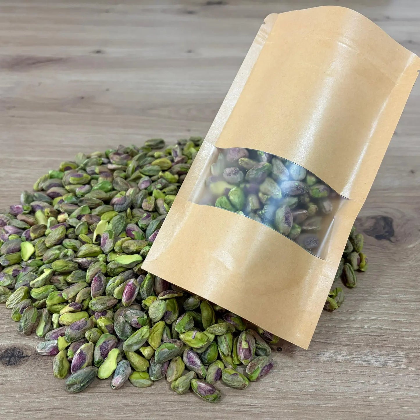 Raw shelled pistachio kernels with natural green and purple hues, displayed next to an eco-friendly kraft paper pouch on a wooden surface.