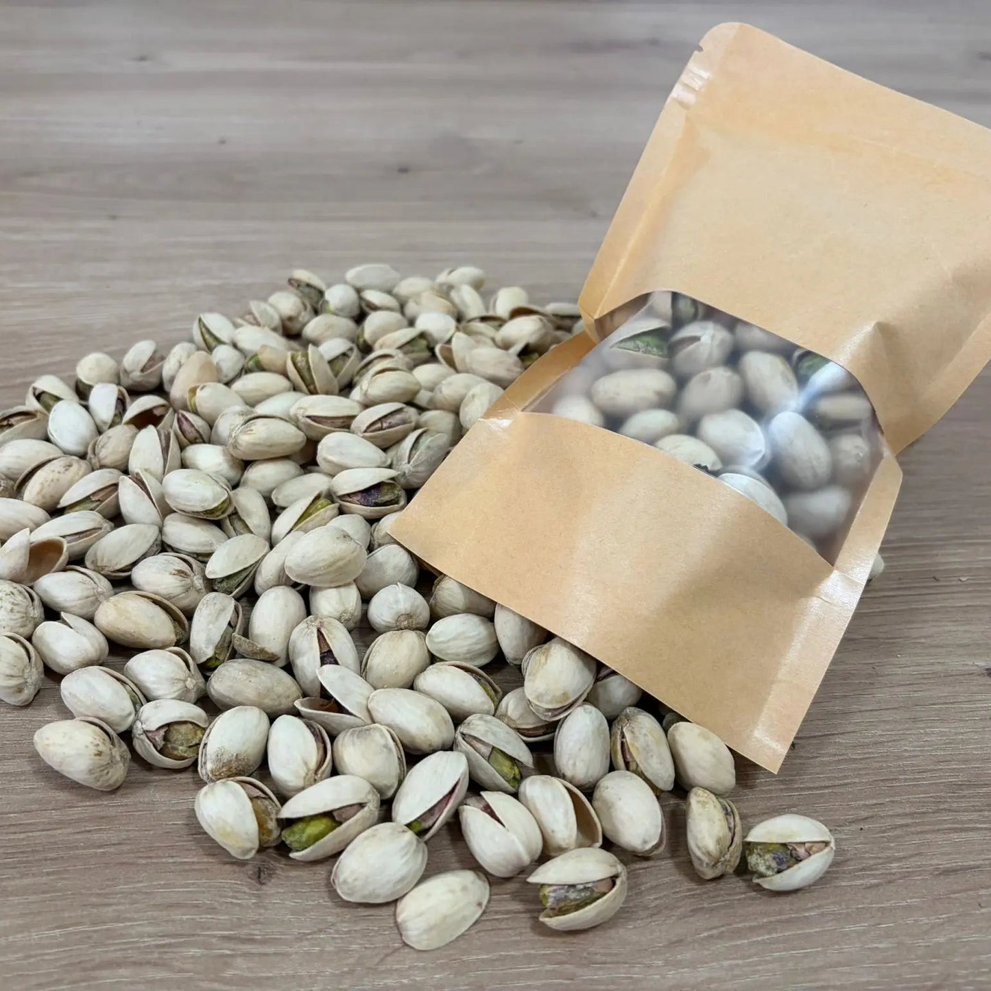 Roasted and salted pistachios in shell, displayed next to an eco-friendly kraft paper pouch on a light wood background.