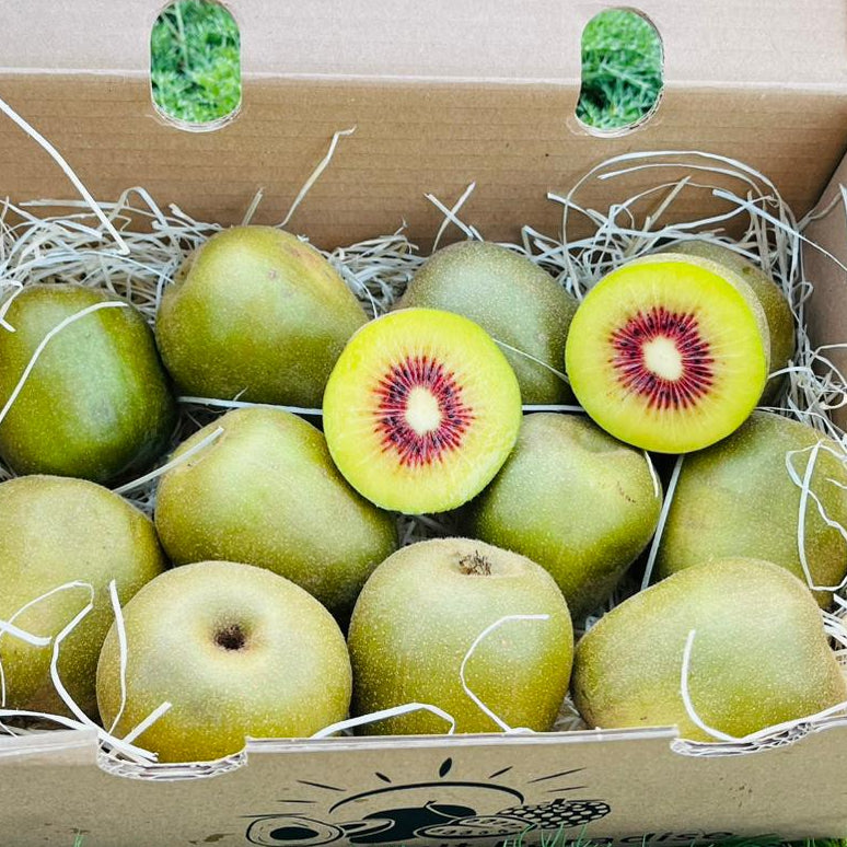 Box of kiwis with one sliced open on a grassy background