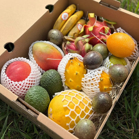 Open cardboard box filled with various fruits on a grassy background