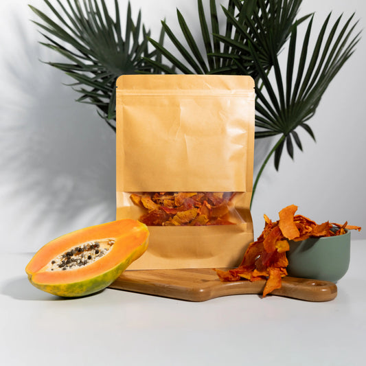 Dehydrated papaya strips in a 100 g kraft pouch and a bowl,
deep orange slices beside a halved fresh papaya