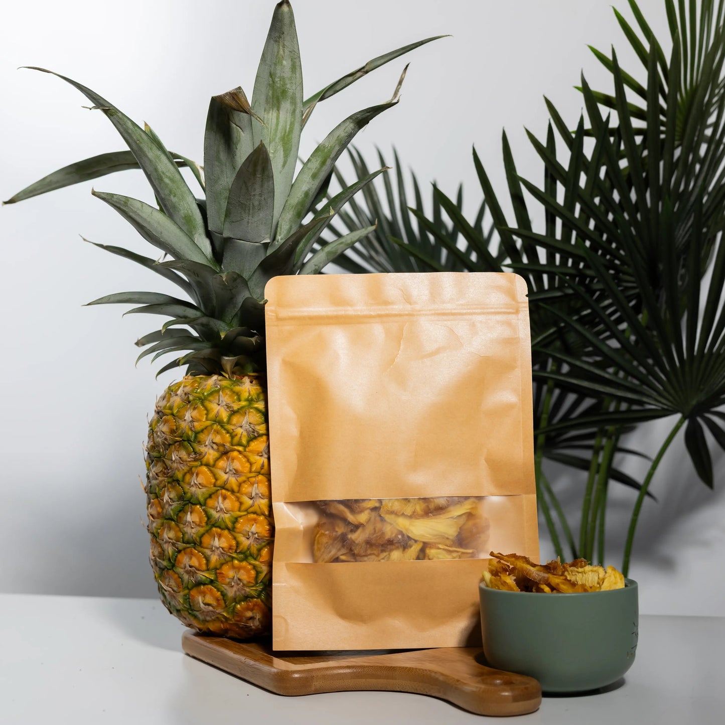 Dehydrated pineapple rings in a 100 g kraft pouch and a bowl,
golden amber slices beside a whole fresh pineapple