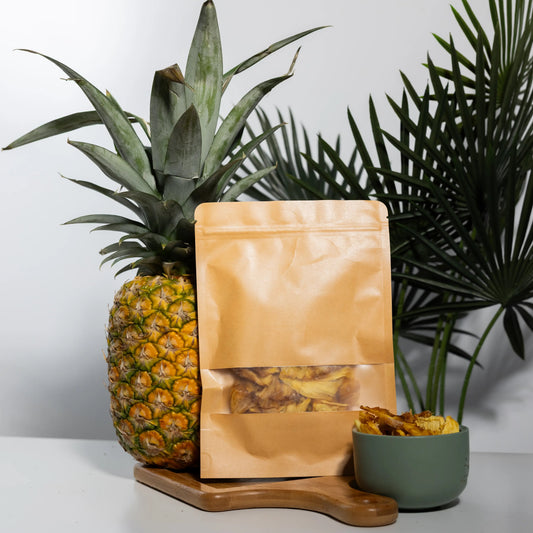 Dehydrated pineapple rings in a 100 g kraft pouch and a bowl,
golden amber slices beside a whole fresh pineapple