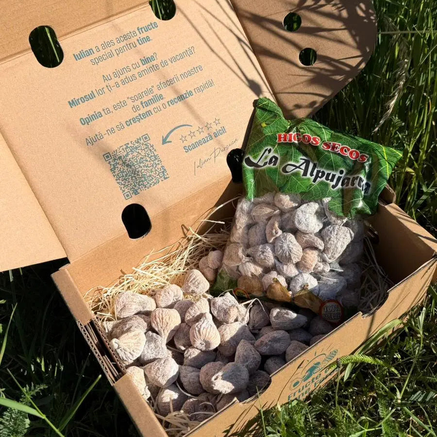Natural dried figs coated in flour, displayed loose and in their original Higos Secos La Alpujarra bag, resting on straw inside a delivery box on green grass.