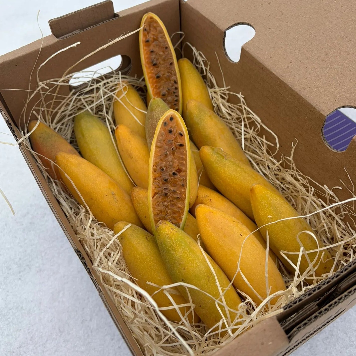 Fresh Curuba (Banana Passionfruit) in a delivery box, sliced open to reveal juicy orange pulp and seeds, exotic fruit delivery by Tropical Fruit Paradise.