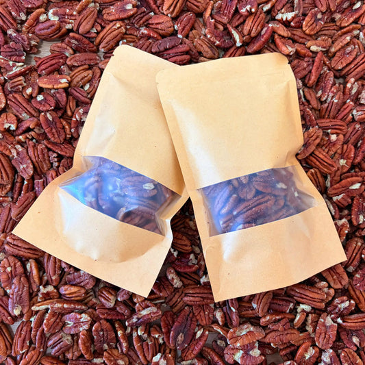 Raw whole pecan nuts in their natural brown shell, displayed on straw inside a Tropical Fruit Paradise delivery box.