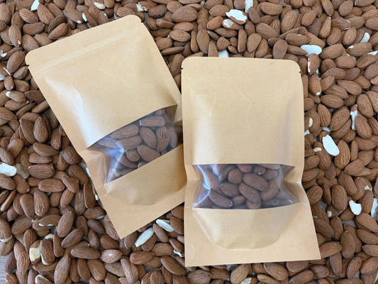 Freshly picked green almonds in their fuzzy outer hull, with one sliced open to reveal the tender nut, in a delivery box on green grass.