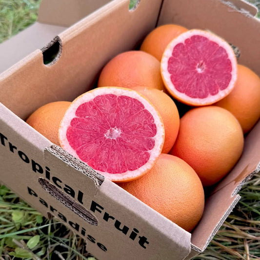 Fresh juicy red grapefruit in a 1.5 kg Tropical Fruit Paradise branded box, with cross-sections showing the vibrant pink pulp, displayed on grass.
