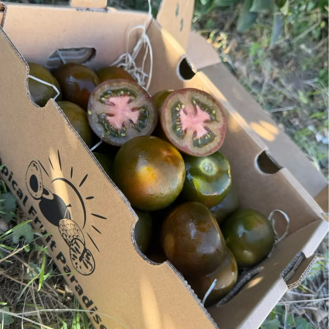 Kumato tomatoes with smooth brown-green skin in a 2 kg Tropical Fruit Paradise box, two halves showing pink flesh, green gel