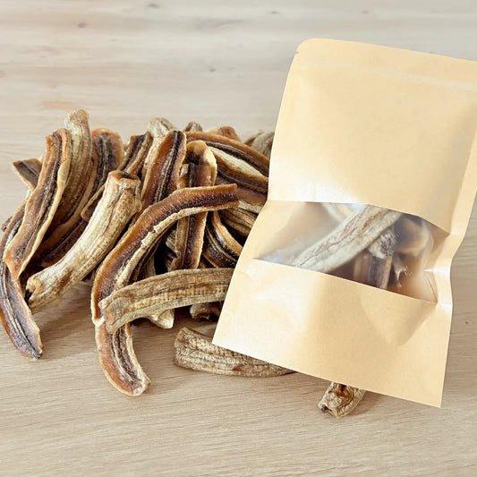 Natural dried banana strips with chewy texture, displayed next to an eco-friendly kraft paper pouch on a light wood background.