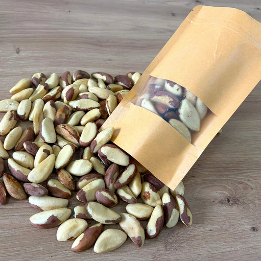 Large raw Brazil nuts, rich in selenium, displayed next to an eco-friendly kraft paper pouch on a light wooden surface.