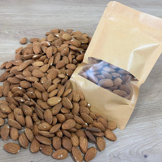 Raw premium California almonds displayed next to an eco-friendly kraft paper pouch on a light wooden surface.