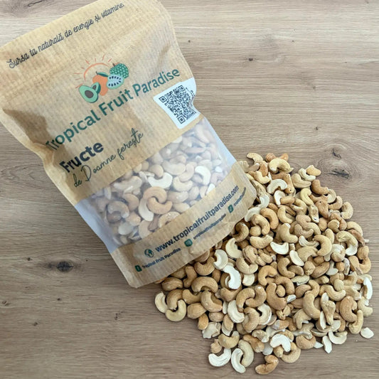 Premium roasted cashews with a warm golden-cream hue, spilling out from a branded Tropical Fruit Paradise kraft pouch onto a light wooden table.