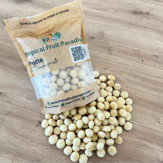 Raw shelled macadamia nut kernels spilled from a branded Tropical Fruit Paradise kraft pouch, displayed on a light wooden background.