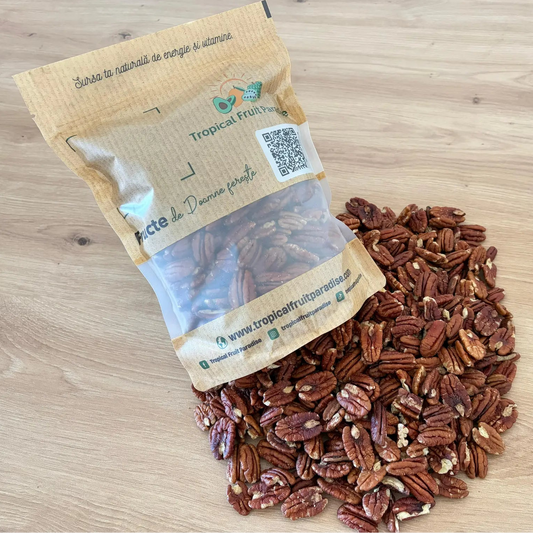 Raw shelled pecan nut kernels with their characteristic wrinkled texture, spilled from a 500g branded Tropical Fruit Paradise kraft pouch, on a light wooden background.