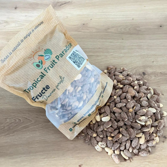Roasted salted almonds with a fine salt dust coating, spilling out of a branded Tropical Fruit Paradise kraft pouch onto a light wooden background.